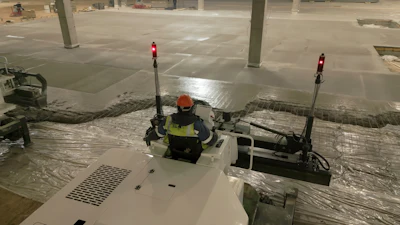 Construction worker in safety gear operating equipment in a parking garage with concrete pillars