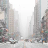 Snow-covered Manhattan street with tall buildings, yellow cabs, and traffic lights during winter weather
