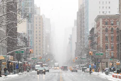 Snow-covered Manhattan street with tall buildings, yellow cabs, and traffic lights during winter weather