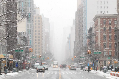 Snow-covered Manhattan street with tall buildings, yellow cabs, and traffic lights during winter weather