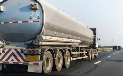 Tanker truck with triple axles transporting liquid cargo on a multi-lane highway.