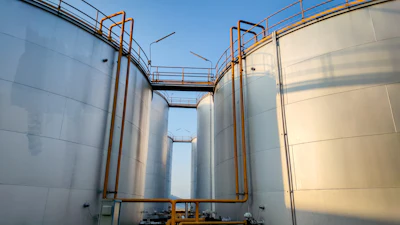 Industrial storage tanks with orange safety railings and metal walkways at a facility