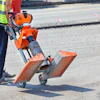Construction worker in high-visibility vest operating orange pneumatic concrete breaker on asphalt road