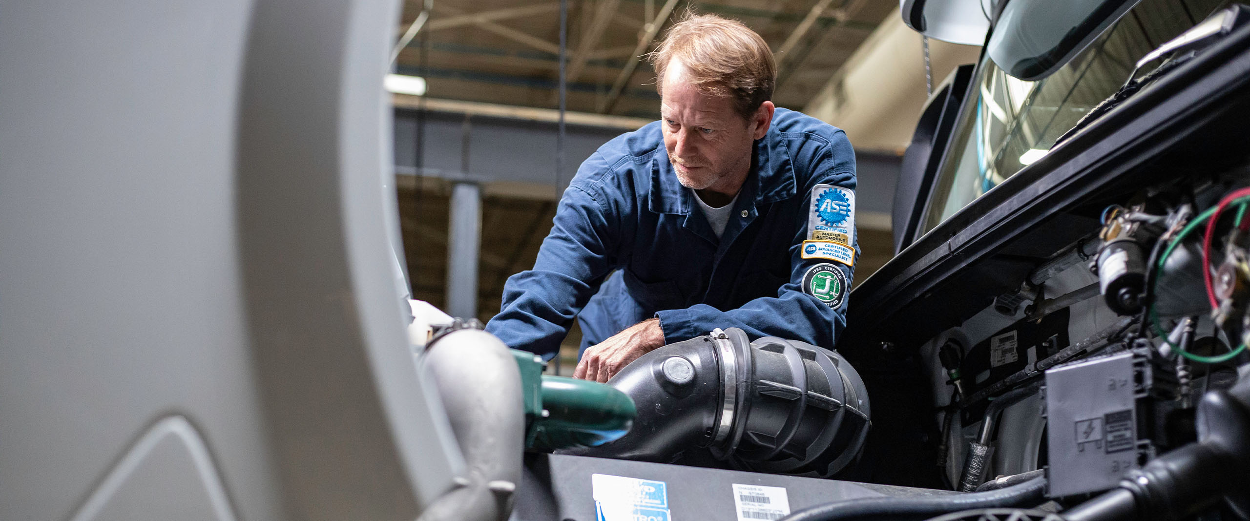 Technician in blue uniform servicing vehicle engine components in an industrial workshop setting