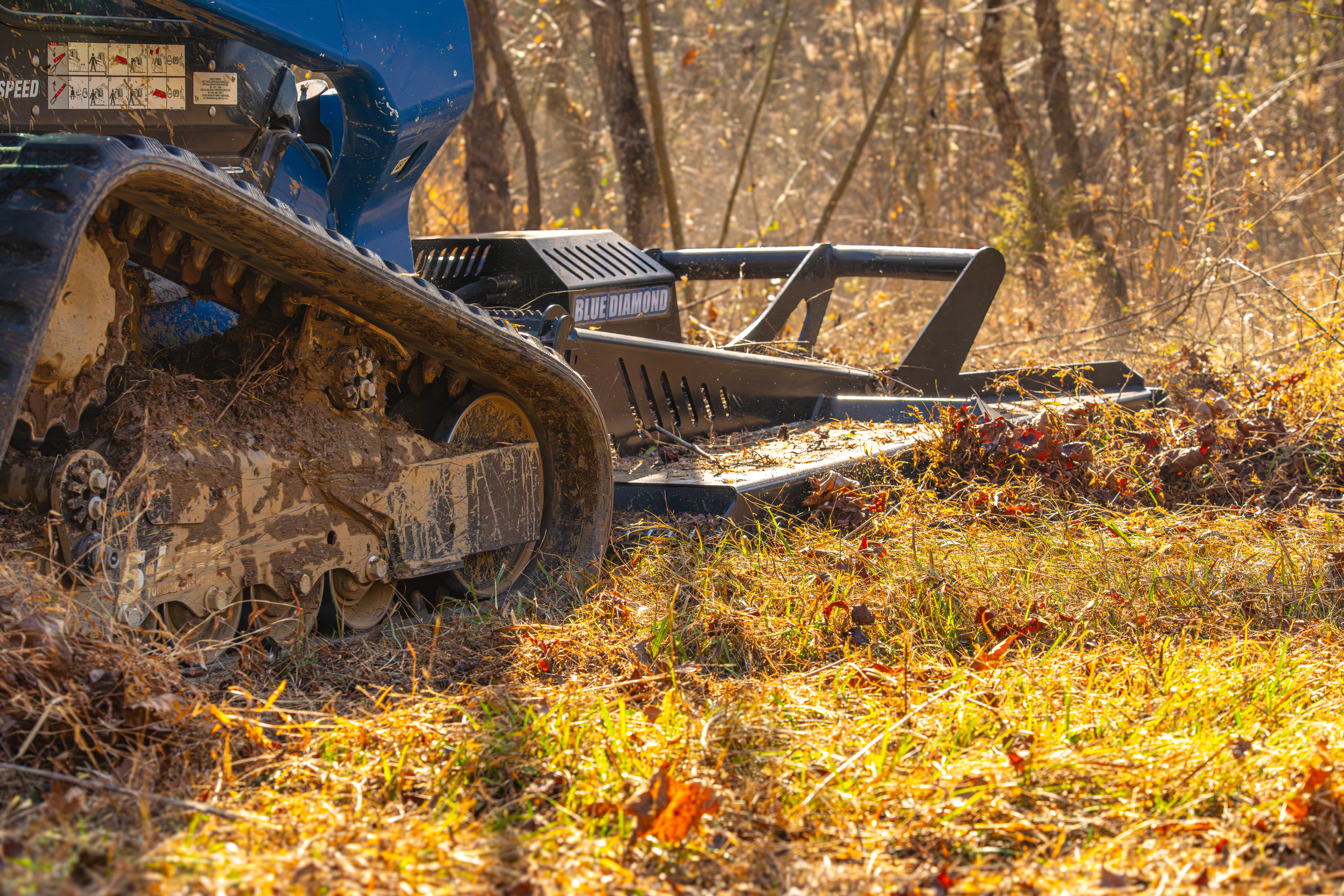 Wood chipper machinery covered in mulch and debris operating in a forest clearing during autumn.