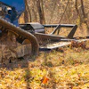 Wood chipper machinery covered in mulch and debris operating in a forest clearing during autumn.