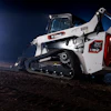 Bobcat T762 compact track loader with white and orange body, illuminated against night sky on dirt terrain