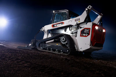Bobcat T762 compact track loader with white and orange body, illuminated against night sky on dirt terrain