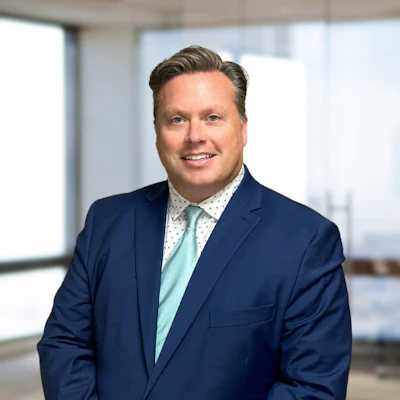 Professional man in navy blazer and light blue shirt smiling in modern office setting