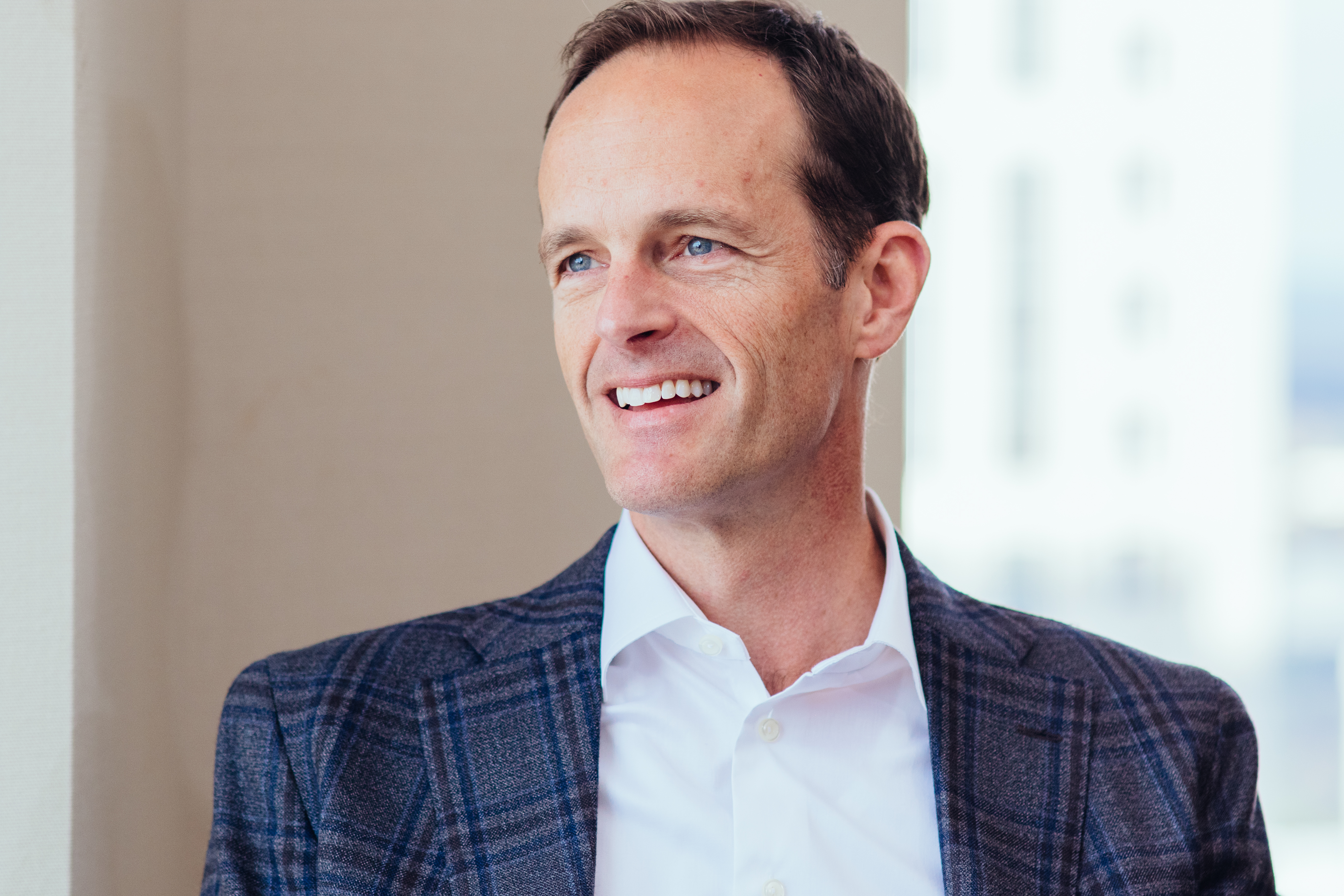 Professional man in navy plaid blazer and white shirt smiling in modern office setting