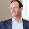 Professional man in navy plaid blazer and white shirt smiling in modern office setting