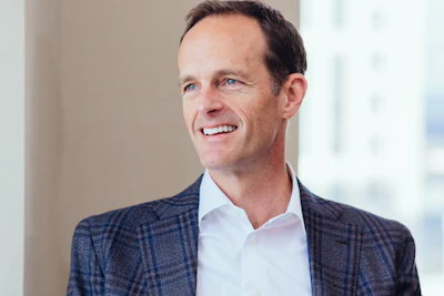 Professional man in navy plaid blazer and white shirt smiling in modern office setting