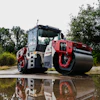 Red and white Dynapac road roller compactor machine reflected in water with trees in background
