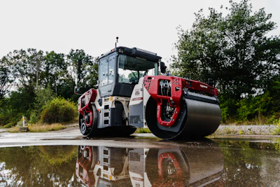 Red and white Dynapac road roller compactor machine reflected in water with trees in background