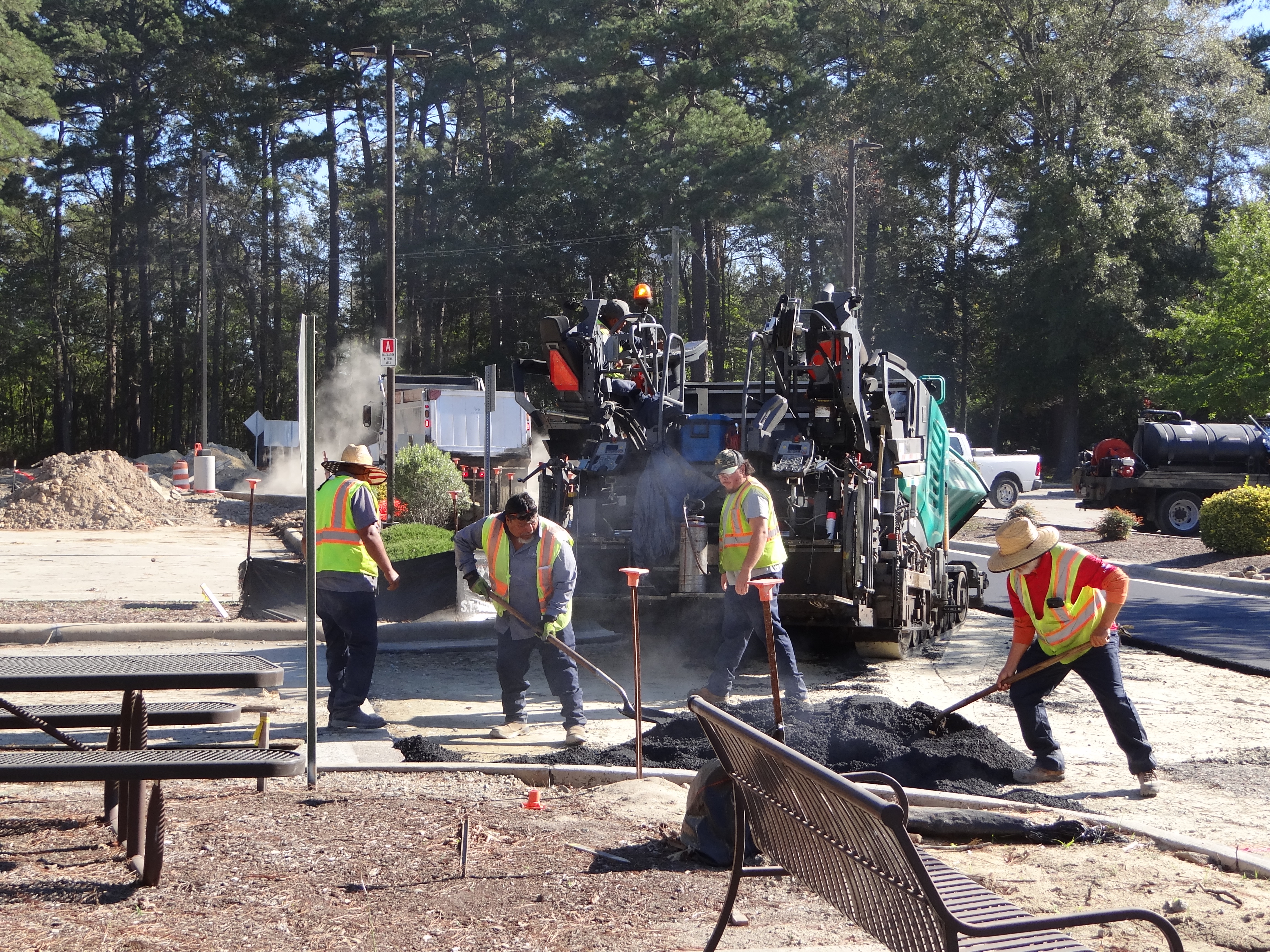 Road construction crew operating asphalt paving equipment with workers in safety vests