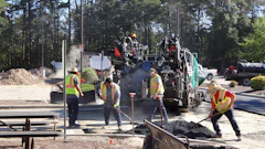Road construction crew operating asphalt paving equipment with workers in safety vests