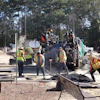 Road construction crew operating asphalt paving equipment with workers in safety vests