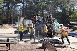 Road construction crew operating asphalt paving equipment with workers in safety vests