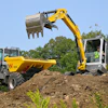 Yellow excavator loading soil into dump truck at construction site with green trees in background
