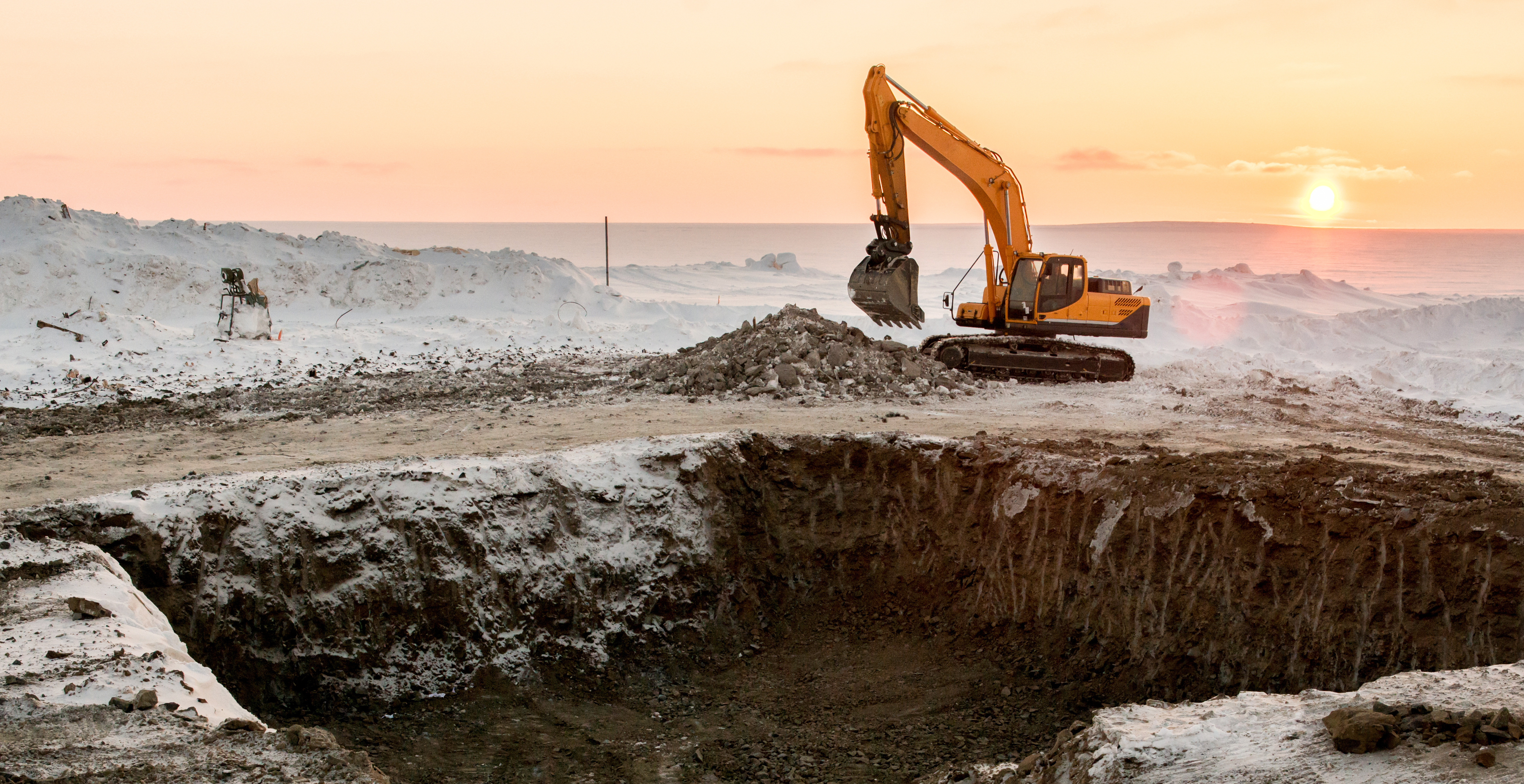 Yellow excavator digging at construction site during golden sunset with misty landscape background