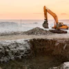 Yellow excavator digging at construction site during golden sunset with misty landscape background