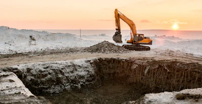 Yellow excavator digging at construction site during golden sunset with misty landscape background