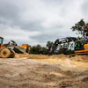 Heavy construction equipment including yellow wheel loader and excavator operating at a dirt job site under cloudy skies