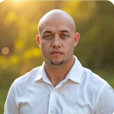 Professional headshot of a bald man wearing a white collared shirt against a blurred golden background Headshot