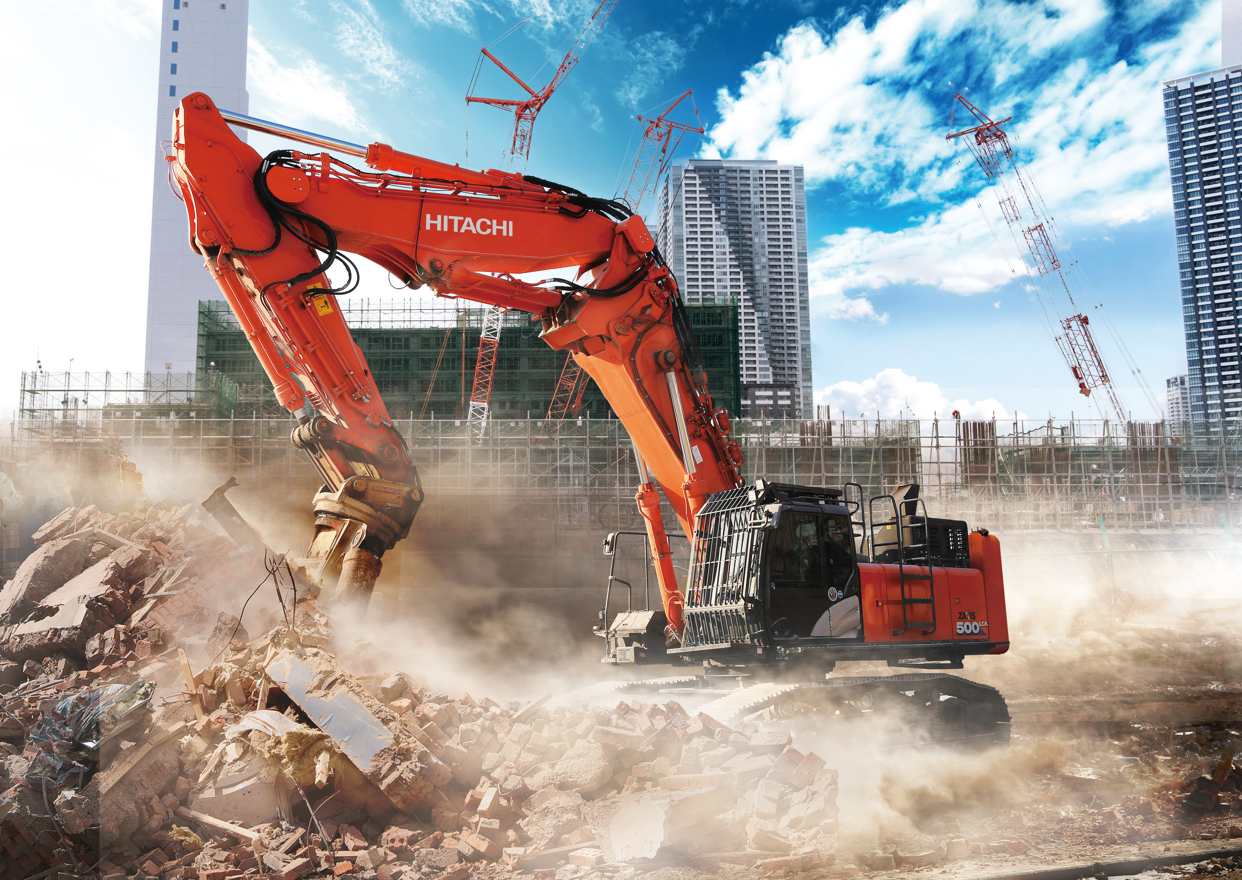 Red Hitachi excavator demolishing building debris on urban construction site with skyscrapers and cranes in background