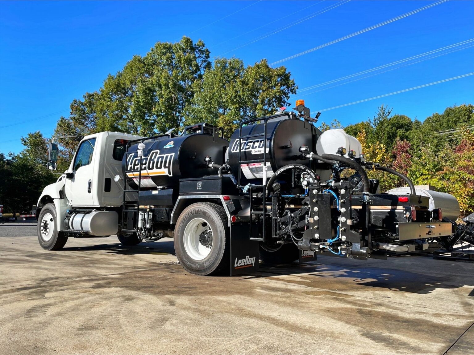 White and black Vac-Tron vacuum truck parked outdoors with blue sky and trees in background