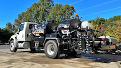 White and black Vac-Tron vacuum truck parked outdoors with blue sky and trees in background