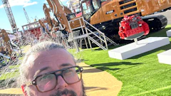 Man with beard and glasses at construction equipment trade show with SANY excavator and machinery in background