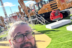 Man with beard and glasses at construction equipment trade show with SANY excavator and machinery in background