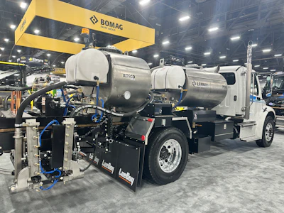 Industrial vacuum truck with dual tanks displayed at trade show under BOMAG overhead crane