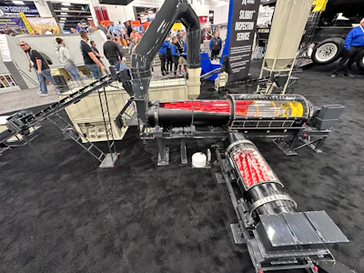 Drag racing vehicle with red and yellow fuel tank displayed at automotive exhibition with spectators and vendor booths