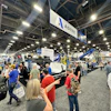 Busy trade show floor with crowds viewing industrial equipment and ASTEC branded displays under bright overhead lighting