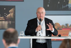 Senior professional speaking at a conference podium with microphone and water glasses