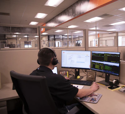 Professional working at dual-monitor workstation in modern office with headphones and technical displays