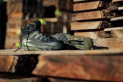 Gray and black HOKA hiking boot displayed on wooden logs in outdoor setting