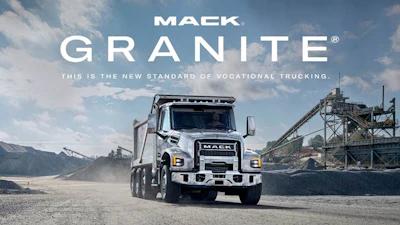 Mack Granite dump truck in industrial quarry setting with mountains and mining equipment in background