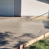 Newly poured concrete driveway with wooden forms and white garage doors visible