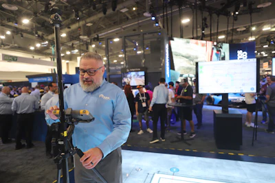 Man demonstrating electric scooter at tech conference with displays and attendees in background