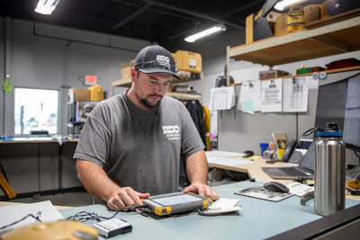 Tradesman in RIDGID-branded cap and shirt working with measuring tools at workshop table