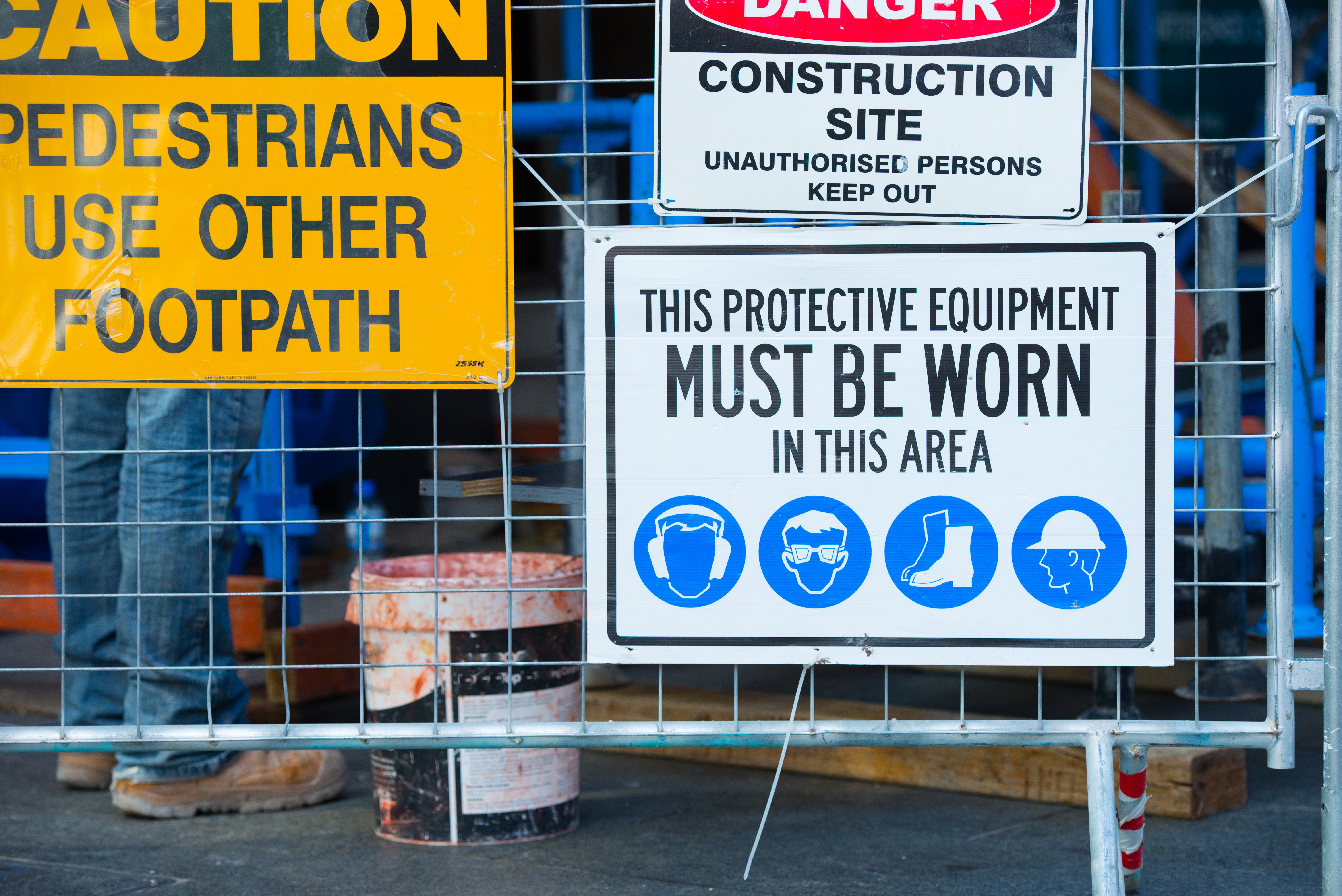Construction site safety signs including pedestrian footpath warning, danger notice, and protective equipment requirements with icons for hard hat, goggles, boots, and safety vest.