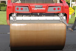Red Dynapac asphalt roller compacting pavement with operator in safety vest nearby