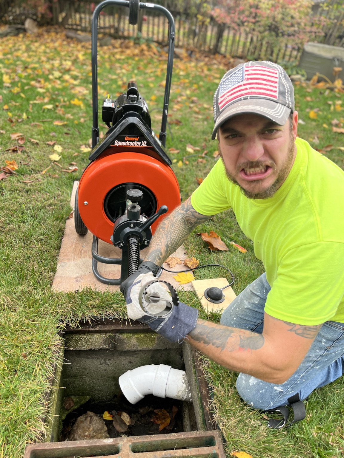 Professional plumber in neon yellow shirt operating orange Speedometer X drain cleaning machine in residential yard