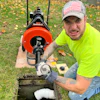 Professional plumber in neon yellow shirt operating orange Speedometer X drain cleaning machine in residential yard