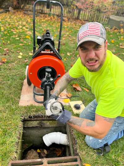 Professional plumber in neon yellow shirt operating orange Speedometer X drain cleaning machine in residential yard