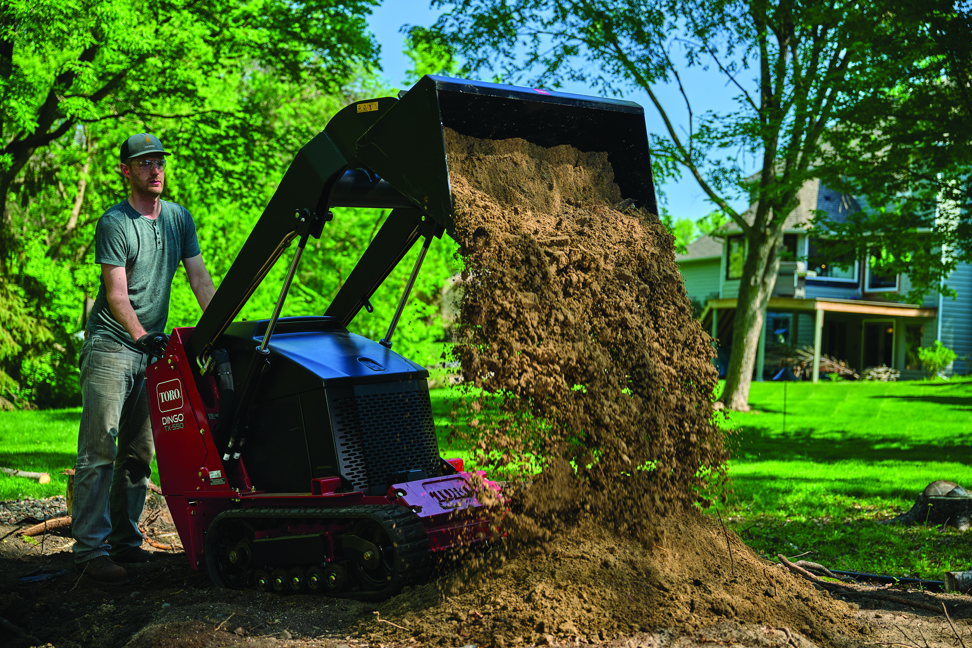 Worker operating red Toro wood chipper, dumping mulch in residential yard with trees