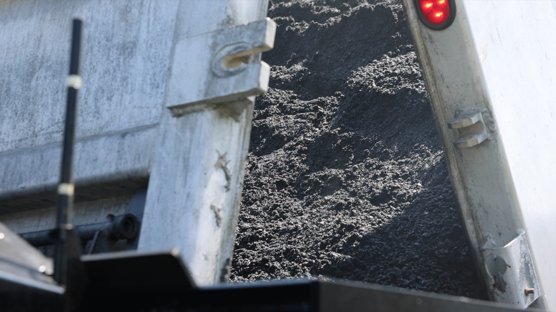 Truck bed filled with dark crushed stone aggregate material with red traffic light visible